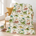 A cream-colored throw blanket with a colorful dinosaur pattern and the brand name 'Caiden' printed repeatedly, draped over a light wood armchair in a bright room.