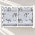 Little Elephant changing pad cover with gray watercolor elephants and the name Cooper on pale blue, shown on a white changing table.