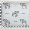 Close-up of Little Elephant crib sheet showing gray watercolor elephants and Cooper in slate blue lettering on a pale blue background.