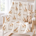 A personalized baby blanket with a repeating pattern of giraffes and the name 'emerson' is draped over a white wooden rocking chair next to a plush stuffed giraffe toy.