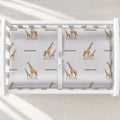 Little Giraffe personalized changing pad cover featuring watercolor adult and baby giraffes and the name Emerson in brown, shown on a white changing table.