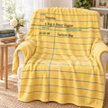 A yellow fleece throw blanket with blue horizontal lines and a lined-paper style writing template design, draped over a beige armchair in a bright, styled living room setting.