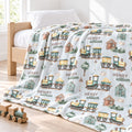 A personalized blanket with a train and house pattern, draped over a wooden bed in a bright, sunlit bedroom. The blanket features the name 'HENRY william' printed repeatedly alongside illustrations of colorful toy trains, small houses, and trees.