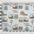 A personalized baby crib mattress cover featuring a repeating pattern of vintage toy trains, small houses, trees, and the names 'HENRY' and 'william' printed in brown text on a pale blue background.