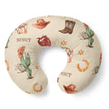 A U-shaped nursing pillow with a western-themed print featuring cacti, cowboy hats, boots, horseshoes, stars, and the word 'SCOUT' on a cream background.