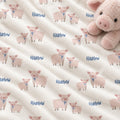 A close-up of a plush cream-colored blanket or quilt with a repeating pattern of pink pigs and the name 'Harlow' in blue script. A matching pink plush pig toy is partially visible in the top right corner.