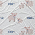 White fabric with a repeating pattern of cartoon pigs and the word 'Harlow' in blue script.