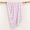 Blush pink personalized swaddle blanket with watercolor bows, tiny sparkles, and the name Charlotte Mae, draped over a wooden branch.