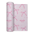 Rolled blush pink personalized swaddle blanket with watercolor bows, tiny sparkles, and the name Charlotte Mae.