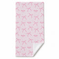 Blush pink beach towel with watercolor bows, tiny sparkles, and the repeated name Charlotte Mae, with a folded corner showing the white reverse.