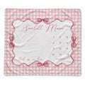 A baby milestone blanket with a pink and white gingham border, featuring a central white panel with a scalloped pink frame, bows, the name 'Scarlett Marie' in script, and a numbered 1-12 timeline for tracking months.