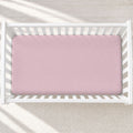 A pink fitted crib sheet with a white polka dot pattern, shown inside a white wooden baby crib on a light textured rug.