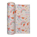 A rolled personalized swaddle blanket and a flat sheet displaying a whimsical unicorn pattern. The design features pastel blue unicorns with orange manesues, pink bows, colorful rainbows, stars, and hearts on a light cream background.