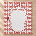 A personalized monthly milestone blanket with a red and white harlequin diamond pattern border, a large white writing area, and a small red star ornament hanging from a metal ring on the left side, shown on a light wood floor.