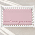 A pink fitted crib sheet with the names 'olivia grace' embroidered in dusty rose script across the front, shown inside a white wooden crib.