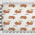 A fitted crib sheet with a repeating pattern of brown sloths sleeping on branches next to yellow crescent moons and small gold stars on a white background. The name 'Sienna' is printed in brown script below each sloth.