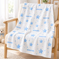 A white baby blanket with light blue stars, dots, and the name 'SEBASTIAN' printed repeatedly, draped over a light wood armchair in a bright room with a teddy bear visible on the left.