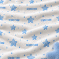 Close-up of a soft white fabric with a repeating blue star and dot pattern, plus the name 'SEBASTIAN' printed in blue across the surface.