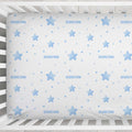 A white fitted crib sheet with a light blue pattern of stars, dots, and the name 'SEBASTIAN' printed repeatedly, shown inside a white wooden crib.
