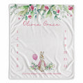 A personalized baby milestone blanket with a watercolor floral border, a bunny illustration, and a numbered countdown from 1 to 12. The blanket is personalized with the name 'Olivia Grace' in pink script at the top.