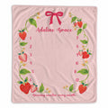 A personalized baby milestone blanket featuring a pink background decorated with a strawberry and green leaf border, a pink bow at the top, and the text 'Adaline Grace' along with a numbered countdown from 1 to 12.