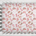 A fitted crib sheet with a western-themed pattern featuring pink cowboy boots, tan hats, brown leopard-print boots, cherries, and the word 'Marvelue' in script, shown inside a white wooden crib.