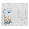 Baby boy milestone blanket featuring a teddy bear, blue balloon, floral moon, and monthly number grid.