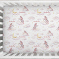 A crib mattress or fitted sheet with a repeating whimsical print of pink and white unicorns on clouds, yellow crescent moons, small gold stars, and the name 'Arabella' in script. The bedding is shown inside a white wooden crib.