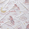 White fabric with a whimsical unicorn print, featuring pastel pink and lavender unicorns on fluffy clouds, a gold crescent moon, small gold stars, and the personalized name 'Arabella' in pink script.