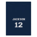 A navy blue blanket featuring the name 'JACKSON' and number '12' printed in white varsity-style lettering with a thin white outline.