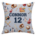 A square throw pillow with a light gray background printed with a baseball-themed pattern of jerseys, bats, helmets, gloves, and popcorn. The center features the text 'CONNOR 12' in navy blue and white.