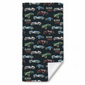 A beach towel with a dark navy background printed with vintage race cars and the personalized name 'OLIVER james' in a repeating pattern. The bottom right corner is folded over to show a white reverse side, set against a plain white background.