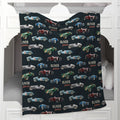 A personalized fleece blanket featuring a vintage race car pattern with the name 'OLIVER James' repeated, draped over a white wooden mantel.