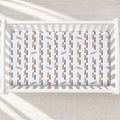 A white crib mattress fitted sheet with a repeating pattern of colorful crayons and the name 'CASEY' in navy blue, shown inside a white wooden crib on a light textured rug.