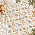 Wildwood Safari blanket personalized with Oliver, spread on white bedding beside a plush lion and an open giraffe picture book.