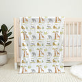 Wildwood Safari personalized baby blanket featuring elephants, giraffes, lions, and zebras, draped over a natural wood crib.