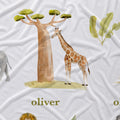 White fabric with a watercolor-style safari print featuring a giraffe, baobab tree, banana leaves, and partial animal illustrations, with the name 'oliver' printed in olive green text.