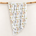 Wildwood Safari swaddle blanket personalized with Oliver, draped over a wooden branch to display the safari animal and tree pattern.