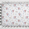 A fitted crib bumper or mattress cover with a winter-themed pattern of polar bears, berries, leaves, and the word 'Winter' in brown script, shown inside a white wooden crib.