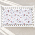 A fitted crib mattress cover with a winter polar bear pattern, shown inside a white wooden crib on a light textured blanket.