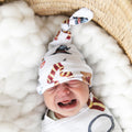 A swaddled baby with a wizard design, featuring a blue and white knit pattern with personalized text, lying in a wicker bassinet.
