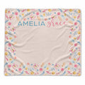 A square personalized blanket with a cream background, decorated with a colorful floral and butterfly border and the names 'AMELIA' and 'grace' printed at the top center.