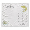 A personalized baby blanket featuring a white background, a cartoon alligator illustration, the name 'Landon' in black script, and a numbered calendar grid from 1 to 12 with the word 'months' written at the bottom.