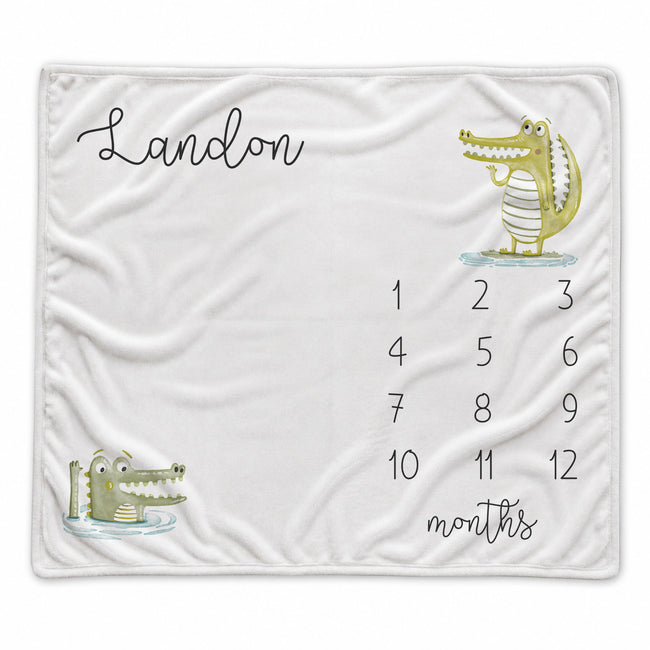A personalized baby blanket featuring a white background, a cartoon alligator illustration, the name 'Landon' in black script, and a numbered calendar grid from 1 to 12 with the word 'months' written at the bottom.