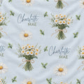 Light blue fabric with a repeating pattern of white daisies, green leaves, and bouquets of daisies, with the personalized text 'Charlotte MAE' printed in blue and green script.