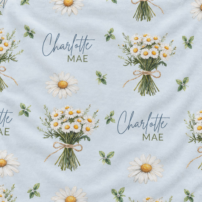 Light blue fabric with a repeating pattern of white daisies, green leaves, and bouquets of daisies, with the personalized text 'Charlotte MAE' printed in blue and green script.