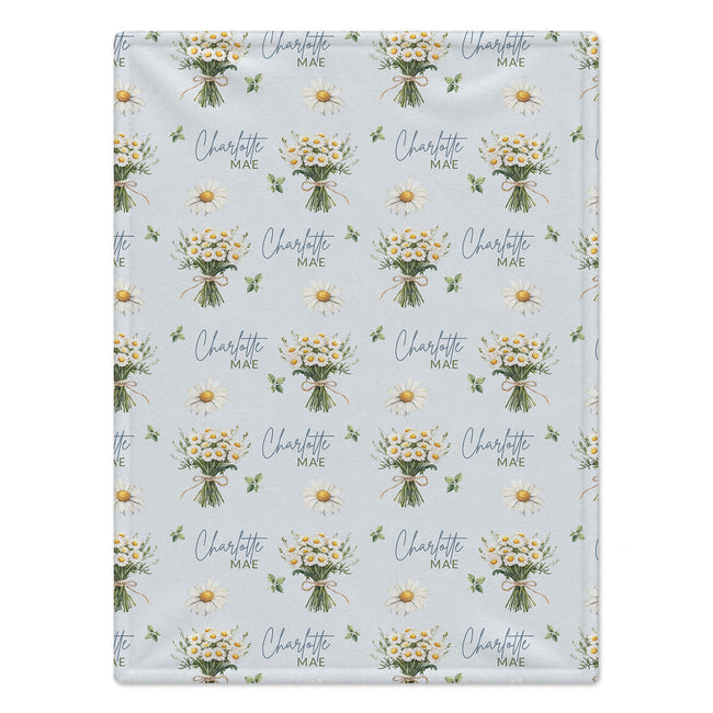Personalized pale blue blanket with white daisy bouquets, green leaves, and the name Charlotte Mae in blue and green lettering.