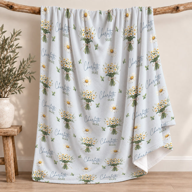 Personalized pale blue blanket with white daisy bouquets, green leaves, and the name Charlotte Mae in blue and green lettering.