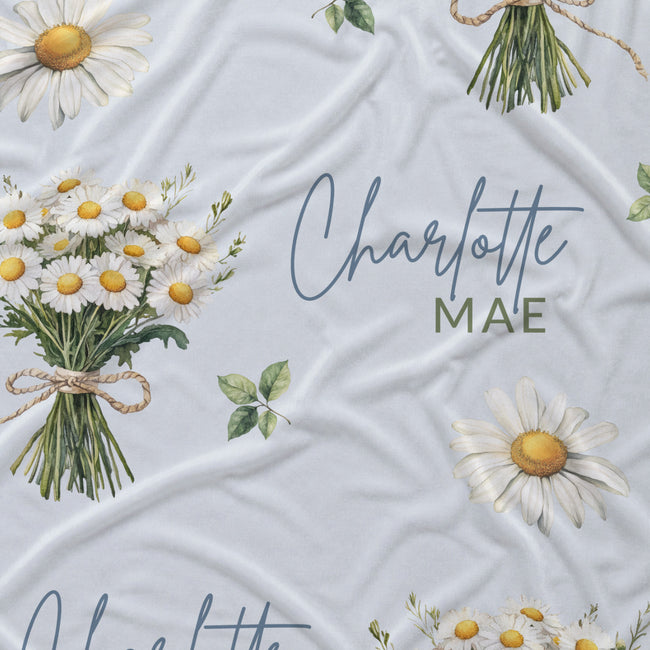 Personalized pale blue fabric with white daisy bouquets, scattered flowers, green leaves, and the name Charlotte Mae.