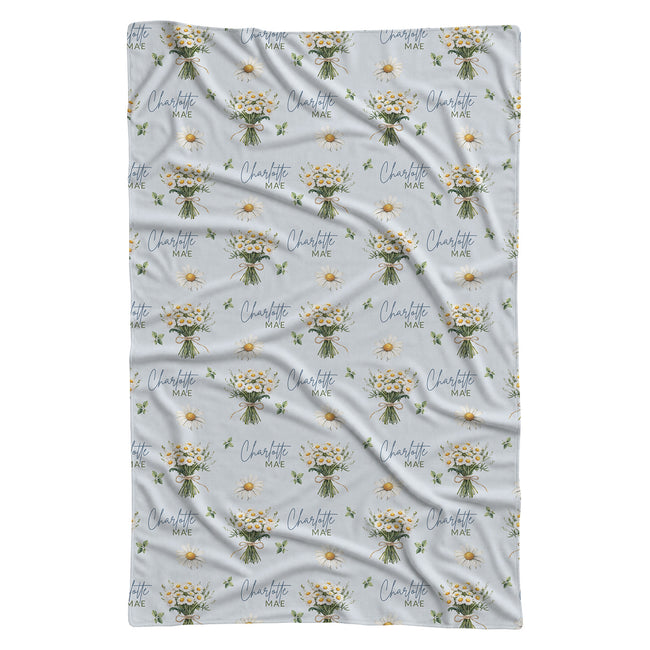 Personalized pale blue swaddle blanket with white daisy bouquets, scattered flowers, green leaves, and the name Charlotte Mae.